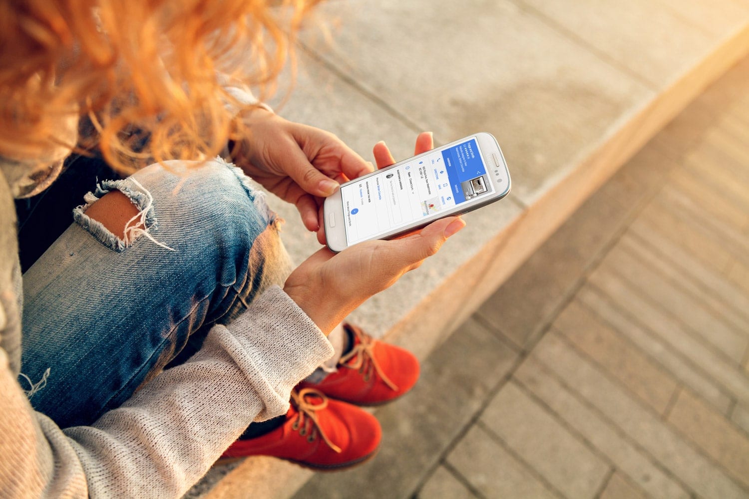 young redheaded woman sitting outdoors looking up local search results on cell phone